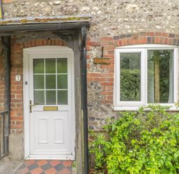 An exterior view of a cottage entrance with a white door and window surrounded by brick and stone walls at Apple Tree Cottage in Shillingstone near Sturminster Newton