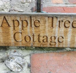 A wooden sign reading Apple Tree Cottage mounted on a brick and stone wall at Apple Tree Cottage in Shillingstone near Sturminster Newton