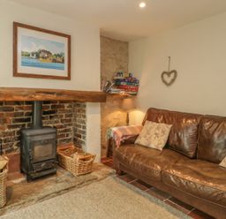 A living room with a wood burner fireplace a leather sofa and a lamp at Apple Tree Cottage in Shillingstone near Sturminster Newton