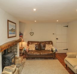 A sitting room with a leather sofa, armchair, wood burning stove, and wooden beam at Apple Tree Cottage in Shillingstone near Sturminster Newton