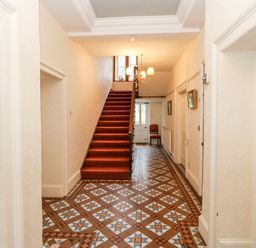 A hallway with patterned tiled floor a red-carpeted staircase a chandelier and a chair near the door at Eden House Edenhall near Penrith