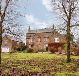 A brick two story house with a blue door and a detached garage in front of a grass yard with two leafless trees at Eden House Edenhall near Penrith
