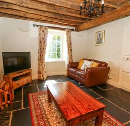 A living room with a leather sofa wooden coffee table television and floral curtains at Penuwch Fach in Aberystwyth