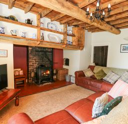 A living room with a wood burning stove wooden beams on the ceiling and leather sofas at Penuwch Fach in Aberystwyth