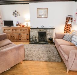 A living room with two sofas a wooden cabinet a fireplace and a small television at Bron Heulog Cottage Llangoed near Beaumaris