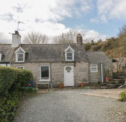 A stone cottage with a gravel driveway and potted plants at Bron Heulog Cottage Llangoed near Beaumaris