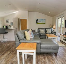 A living room with grey leather sofas and wooden tables at Cartmel Lodge in Allithwaite near Grange-over-Sands