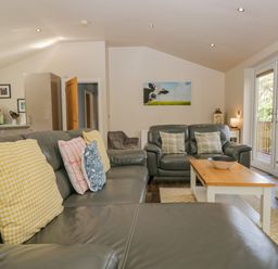 A living room with leather sofas and colorful cushions a coffee table and a wall painting at Cartmel Lodge in Allithwaite near Grange-over-Sands