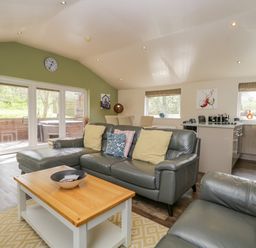 A living room with grey leather sofas and a wooden coffee table next to a dining area and kitchen at Cartmel Lodge in Allithwaite near Grange-over-Sands
