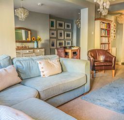 A living room with blue sofas a brown armchair a dining table with chairs a sideboard with sunflowers and pictures on the wall at Craft Cottage Beer near Seaton