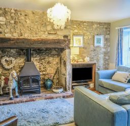A living room with stone walls a wood stove a rocking horse and blue sofas at Craft Cottage in Beer near Seaton