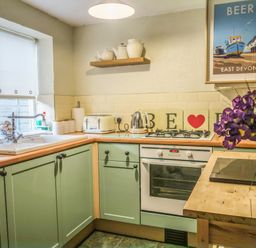 A kitchen with green cabinets a white oven kettle and toaster a shelf with teapots and a framed poster on the wall at Craft Cottage in Beer near Seaton
