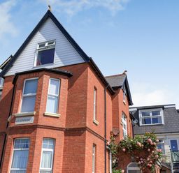 A red brick house with multiple windows and a stairway with flowers in front at Glenwood in Woolacombe