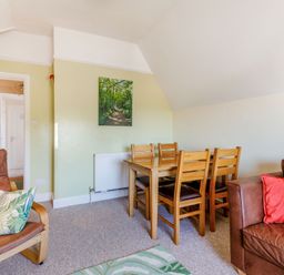 A living and dining area with wooden dining table and chairs leather seating with cushions and a wall painting at Glenwood in Woolacombe