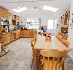 A kitchen with wooden cabinets a dining table with chairs and a rocking chair at Ty Gwynn in Tanygrisiau