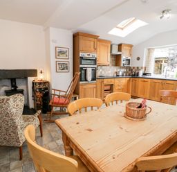 A kitchen and dining area with wooden cabinets a dining table with chairs a floral armchair and a rocking chair at Ty Gwynn in Tanygrisiau