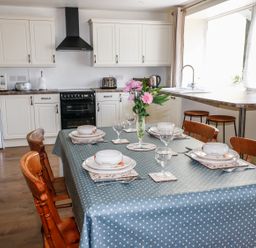 A kitchen with a dining table set with plates and bowls and a vase with flowers at Marsh Cottage in North Molton