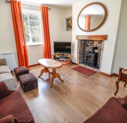 A living room with a wooden coffee table a TV on a stand a fireplace with a mirror above orange curtains and sofas at Marsh Cottage in North Molton