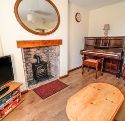 A living room with a fireplace stove television piano coffee table and a sofa at Marsh Cottage in North Molton