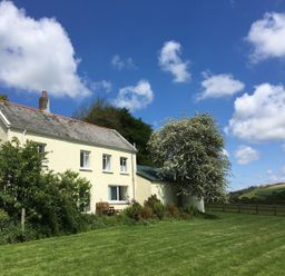 A two-story cream house with a lawn and trees under a blue sky at Marsh Cottage in North Molton