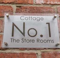 A metal sign on a brick wall reading Cottage No 1 The Store Rooms