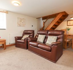 A living room with brown leather sofa and armchair beside wooden staircase and dining table with chairs at Garreg Wen Isaf Bach in Penygroes near Caernarfon