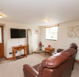 A living room with brown leather sofas wooden door and TV on the wall at Garreg Wen Isaf Bach in Penygroes near Caernarfon