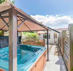 An outdoor hot tub with a canopy and wooden fencing beside a paved walkway at Willow Cottage in Ulrome near Skipsea