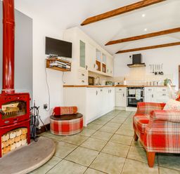 A kitchen with white cabinets red plaid armchair a red wood stove and a mounted television at Willow Cottage in Ulrome near Skipsea