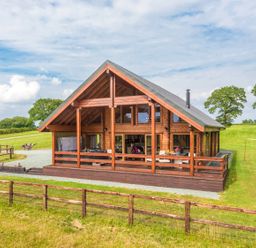 A wooden cabin with large windows and a deck in a grassy field at Hampton Lodge in Ellesmere