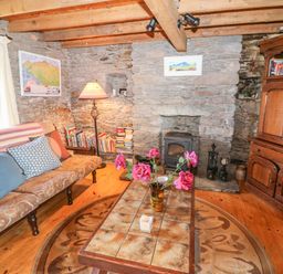 A living room with a tiled coffee table with flowers on it a stone fireplace a wooden cabinet and a sofa with cushions at An Nead in Ballinknockane near Dingle County Kerry