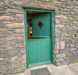 A green half door with the top half open and a stone wall surrounding it at An Nead in Ballinknockane near Dingle County Kerry