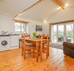 A dining area with wooden table and chairs next to a kitchen with washing machine and sink in an open living space at Vine Cottage in St Ewe near Sticker