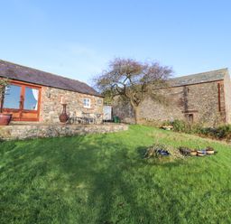 A stone building with a patio table and chairs on a raised stone terrace and grass lawn at Sonya's Cottage in Anthorn Solway Firth