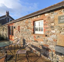 A stone exterior wall with window and door and outdoor table and chairs at Sonya's Cottage in Anthorn Solway Firth