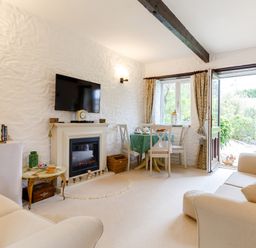 A sitting room with sofas a television above a fireplace and a dining table near an open door at Poldark Cottage in East Taphouse