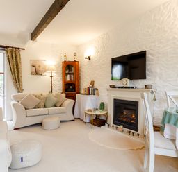 A living room with sofas a fireplace a wall mounted tv and a dining table at Poldark Cottage in East Taphouse