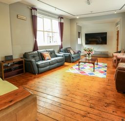 A living room with multiple sofas a wooden floor a coffee table with flowers and a mounted television at Mountain View in Penmaenmawr