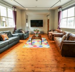 A living room with sofas around a wooden table with flowers a colorful rug and a wall mounted TV at Mountain View in Penmaenmawr