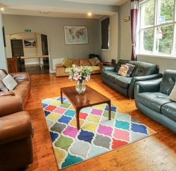 A seating area with multiple sofas a wooden coffee table with a vase of flowers and a colorful patterned rug at Mountain View in Penmaenmawr