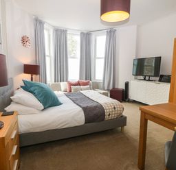 A bedroom with a bed a sofa a wooden table a TV cabinet and a window with curtains at Y Castell Apartment 1 in Criccieth