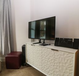A television on a white cabinet next to a window with gray curtains in a room at Y Castell Apartment 1 in Criccieth
