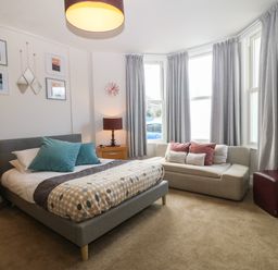 A bedroom with a bed, sofa, bedside tables, lamps, and framed pictures at Y Castell Apartment 1 in Criccieth