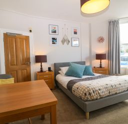 A bedroom with a bed sofa wooden table two bedside tables with lamps and wall art at Y Castell Apartment 1 in Criccieth