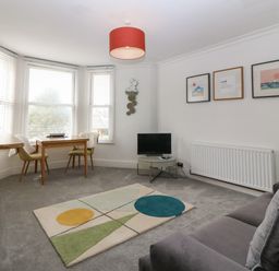 A living room with a gray sofa a small TV on a round table a rectangular dining table with two chairs and a geometric rug at Y Castell Apartment 2 in Criccieth