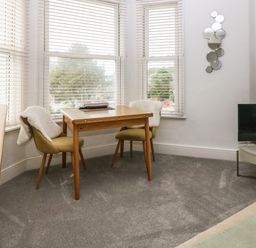 A room with a wooden table and two chairs with white throws near windows with blinds a round table with a television and a wall decoration with round mirrors at Y Castell Apartment 2 in Criccieth