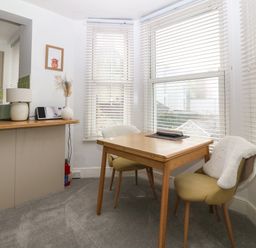 A dining area with a wooden table and two chairs next to windows with blinds at Y Castell Apartment 2 in Criccieth