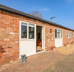 A brick exterior of a house with white doors and windows and a pair of boots outside at Sunnyside Cottage in Blackborough End near King's Lynn
