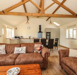An open living room and kitchen with brown sofas and wooden beams at Sunnyside Cottage in Blackborough End near Kings Lynn
