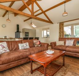 A living room with brown sofas and a wooden coffee table in an open kitchen area at Sunnyside Cottage in Blackborough End near Kings Lynn
